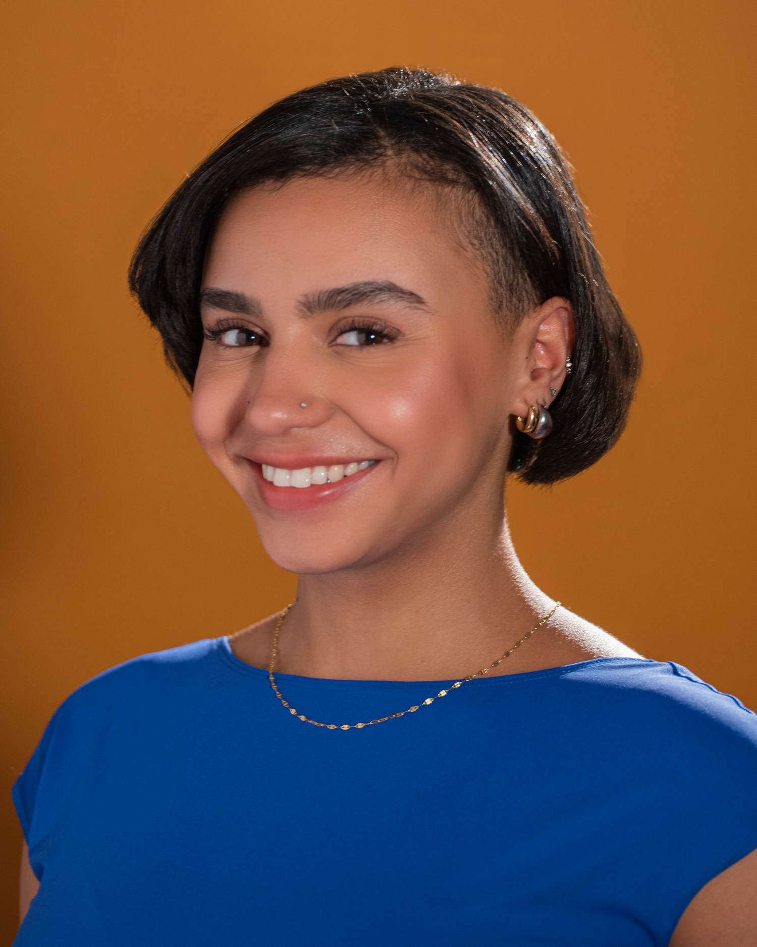 Professional headshot with short dark hair against orange backdrop wearing blue.