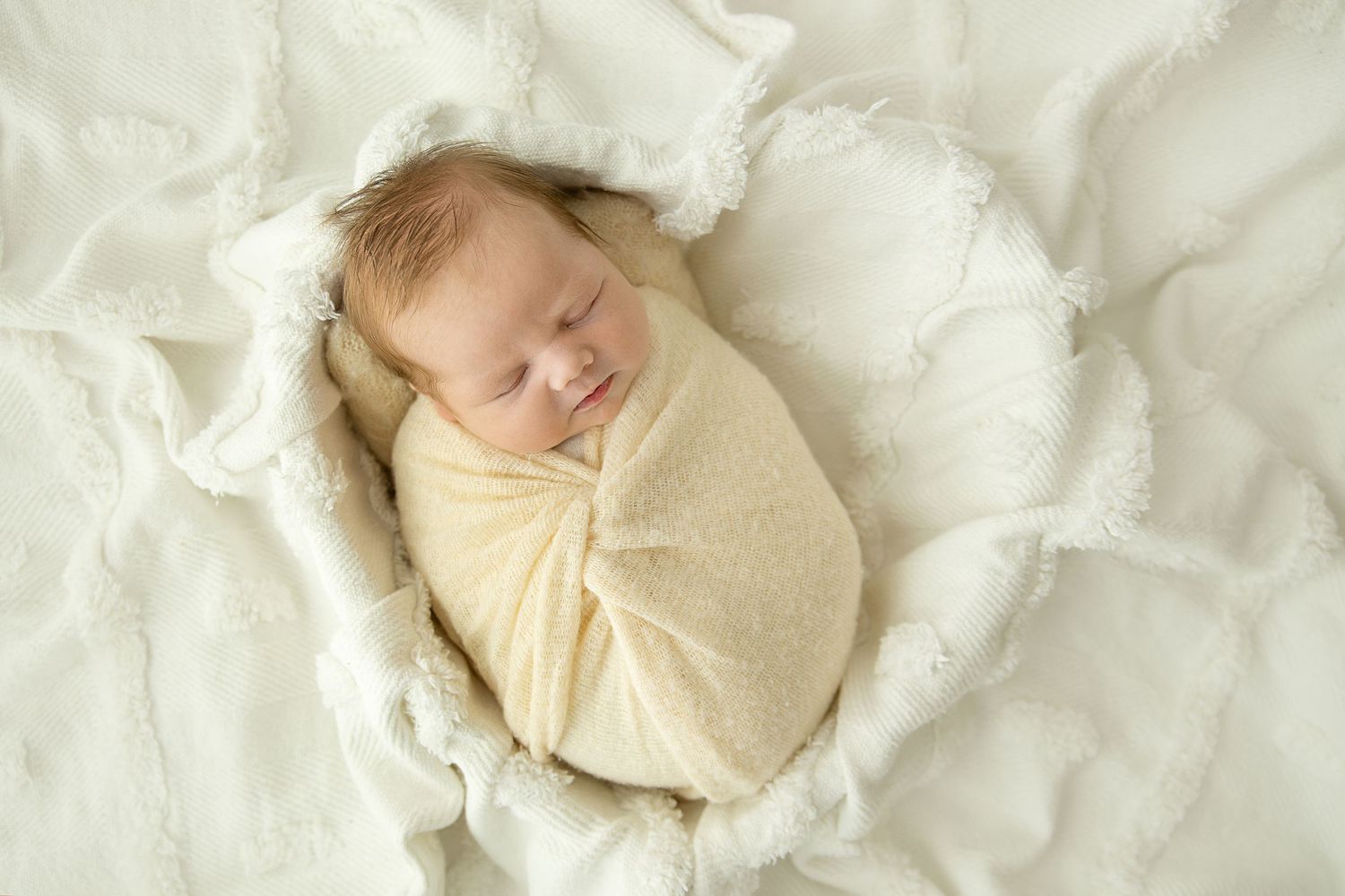 Baby girl all wrapped in a cream wrap placed in heart shaped prop while sleeping.
