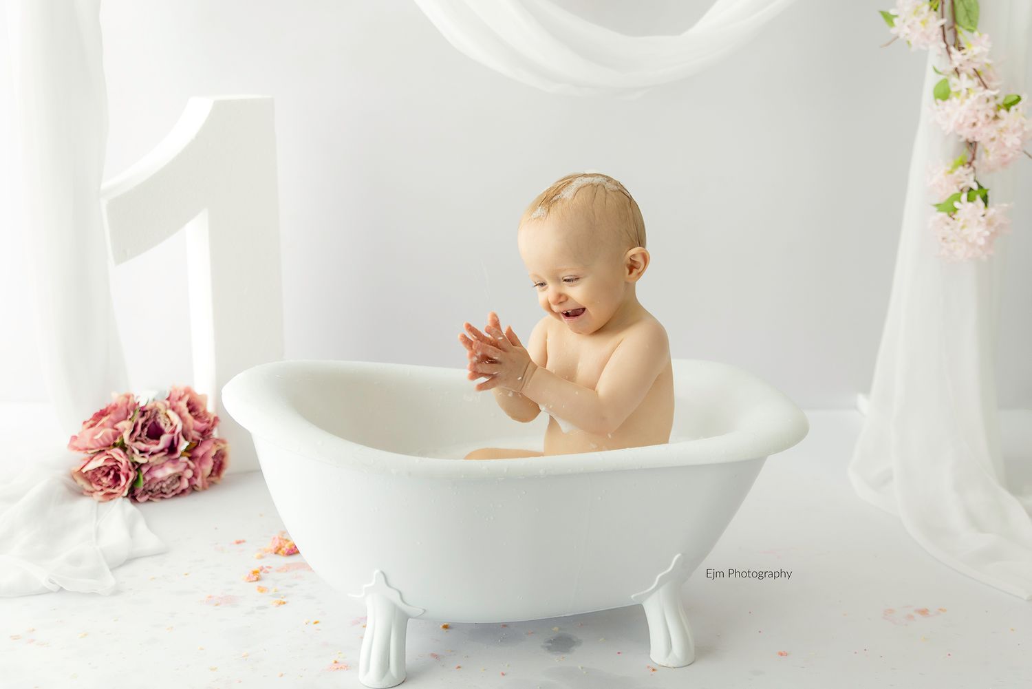 Baby laughing and clapping while sitting in a cake smash photo set up, in a bath prop.
