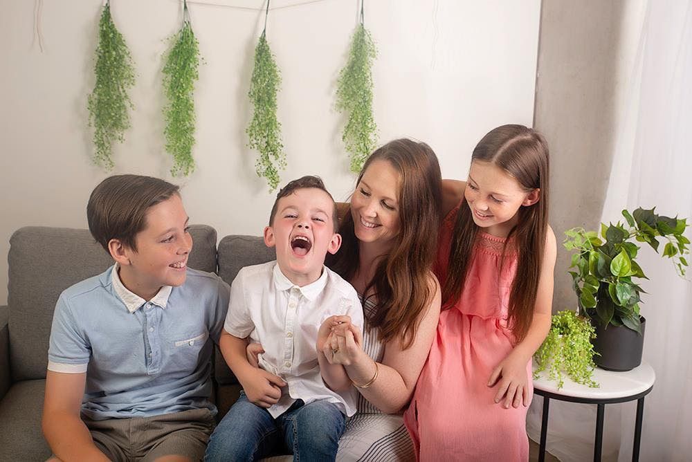 Family photo of mum, two sons and one daughter all looking at youngest while he is laughing a lot.