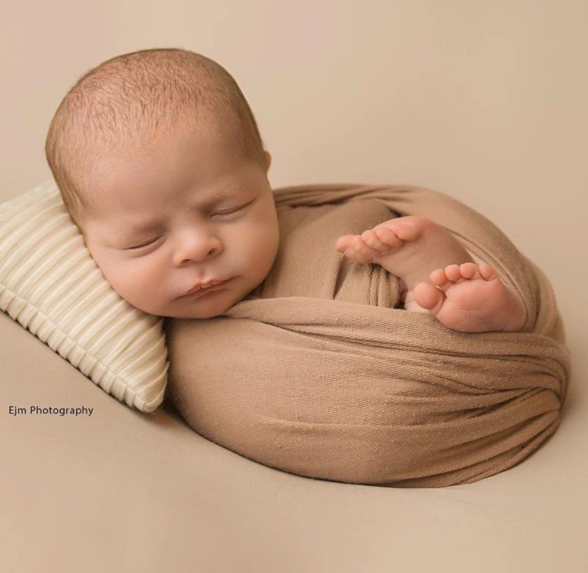 Newborn baby wrapped up snuggly placed on a pillow in a cute brown setup.
