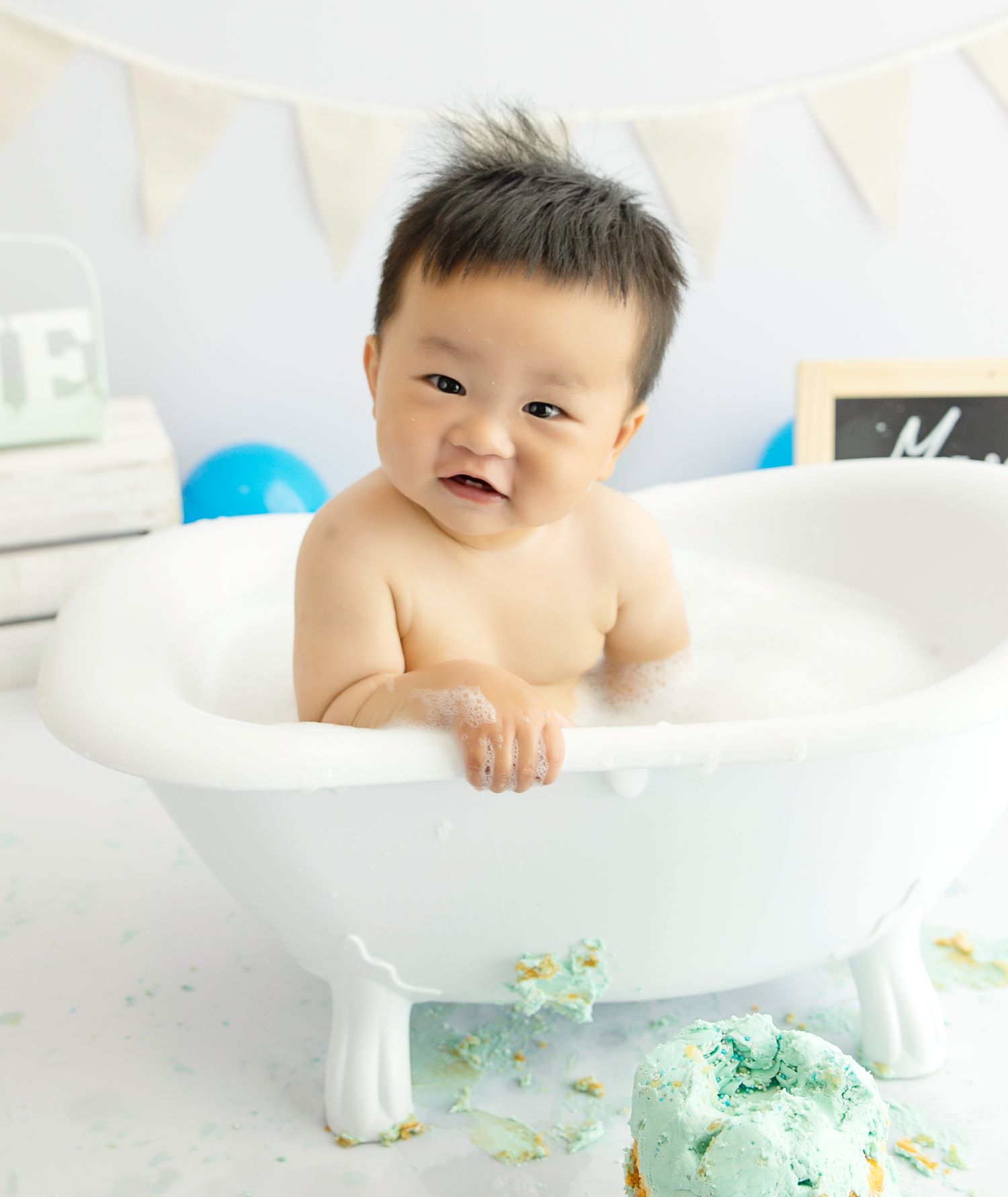 Baby in a bubble bath prop with cake near it. Smiling happily.