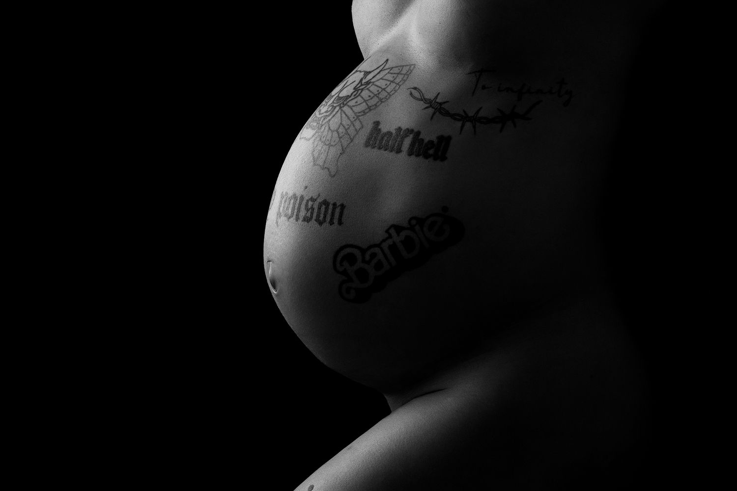 Black on white shot of pregnant belly With tattoos on it, using rim lighting.