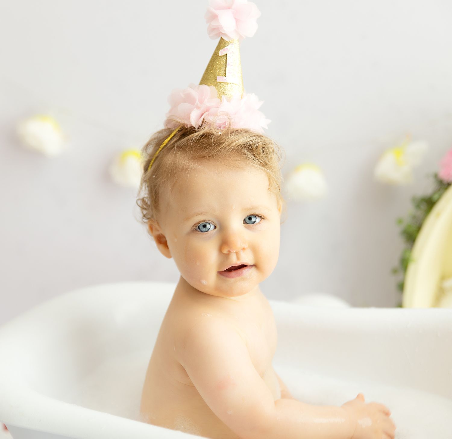 Baby girl sitting in bubble bath prop with a 1 hat on her head for first birthday shoot.