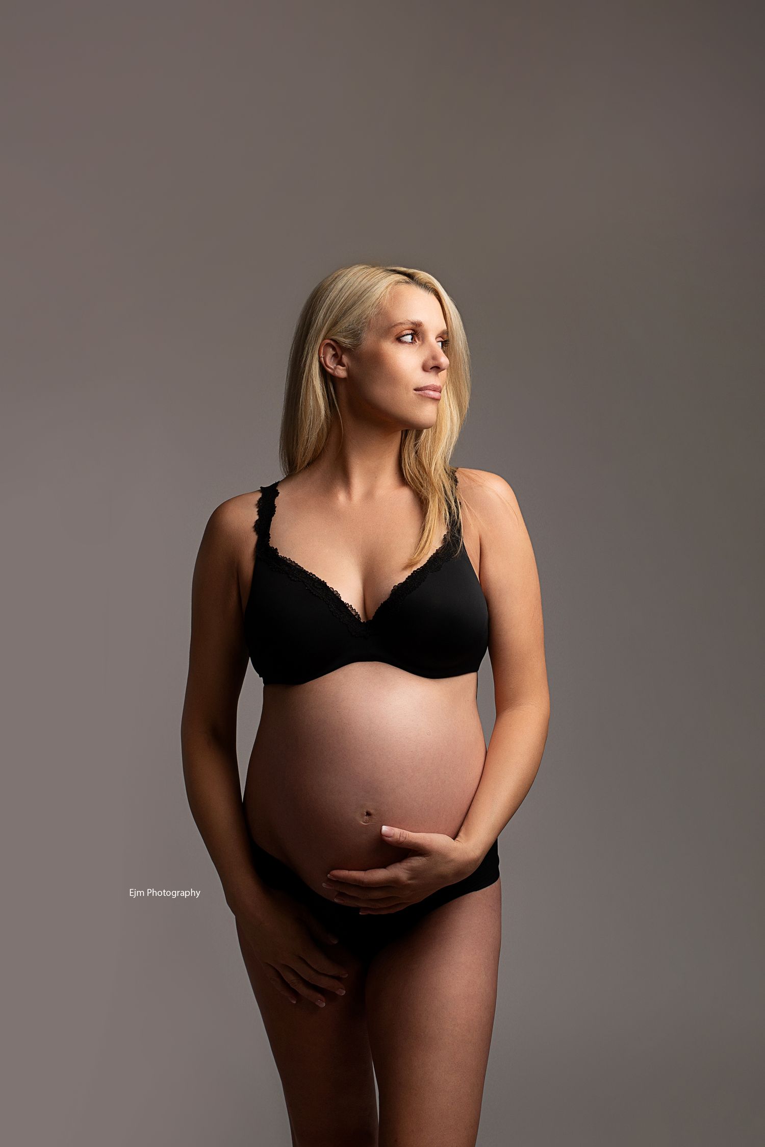 Pregnant lady in underwear holding her belly while looking away. Soft beautiful lightning.