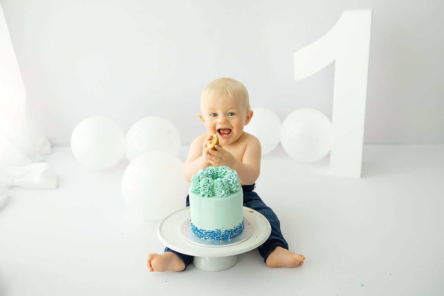 Baby sitting in front of blue cake for cake small photo. All white setup with a large 1 prop.