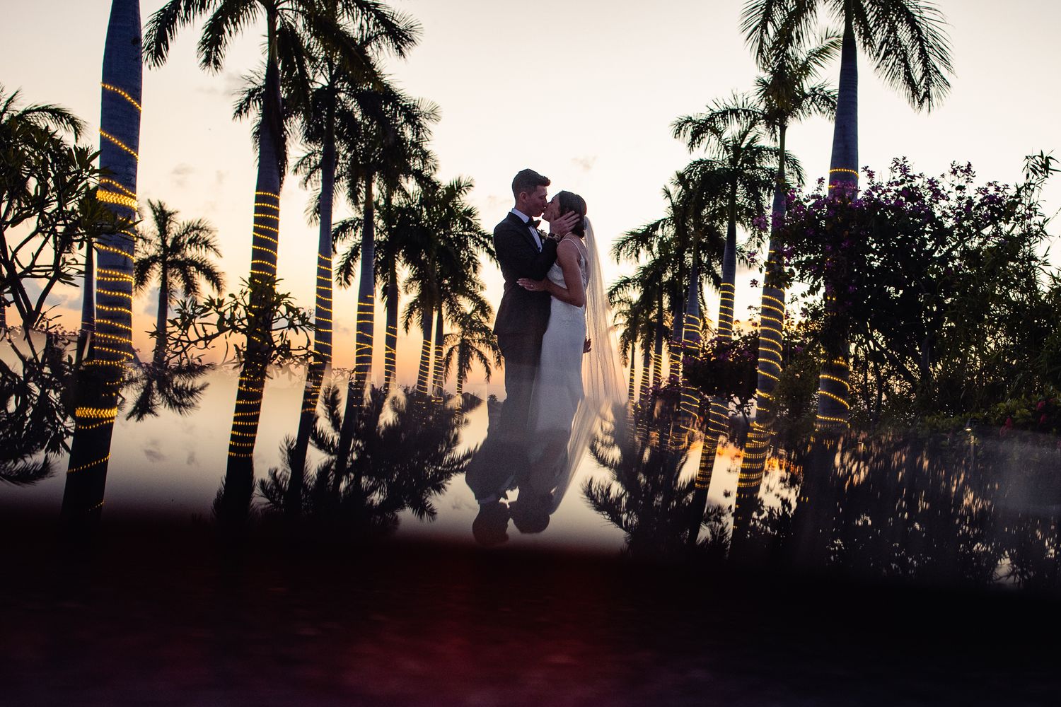 Couple sharing romantic kiss at sunset surrounded by tall palm trees, Cancun Wedding Photographer, Destination Wedding Cancun,
