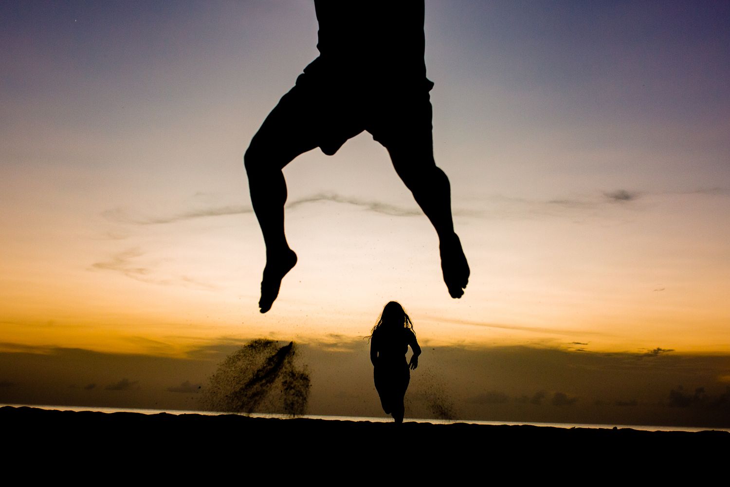 Silhouette of person jumping at sunset with another figure walking in golden hour light on a scenic overlook.