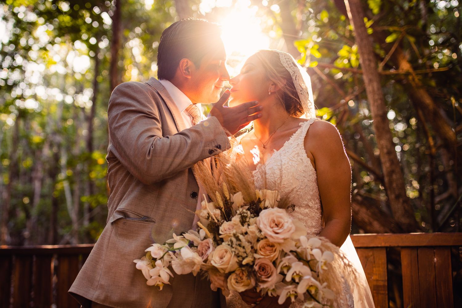 Bride and groom share a romantic moment in sunlit forest, bride holding lush blush floral bouquet.
