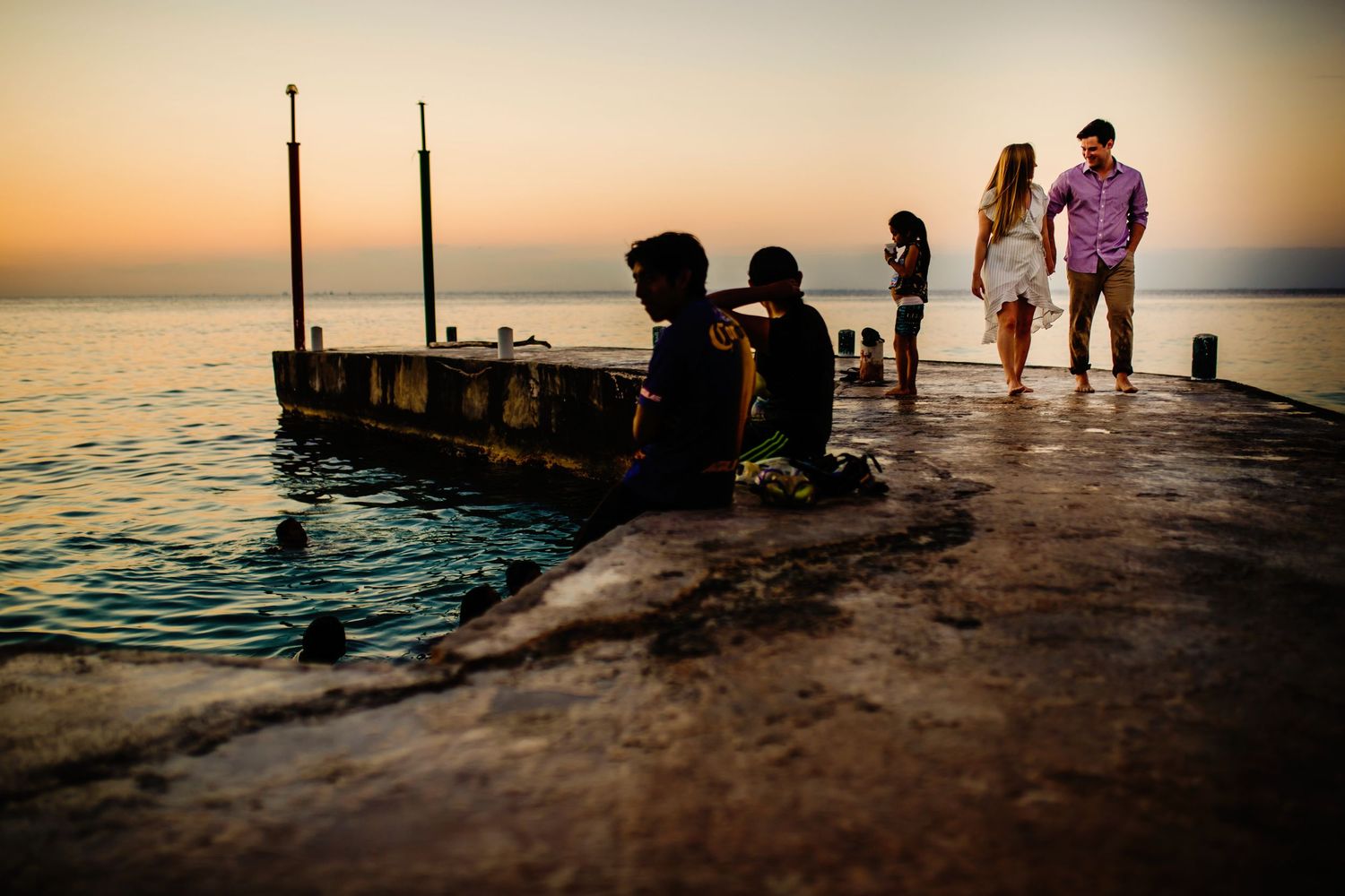 Silhouettes of people gather on a wooden pier at sunset while enjoying the tranquil ocean views.