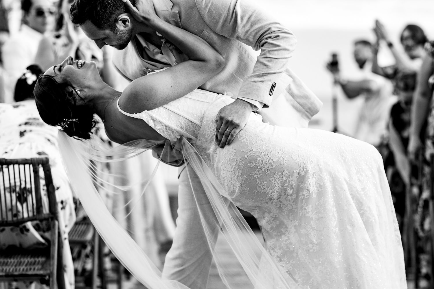 Bride and groom share a romantic dip kiss during their outdoor beach wedding ceremony in black and white.