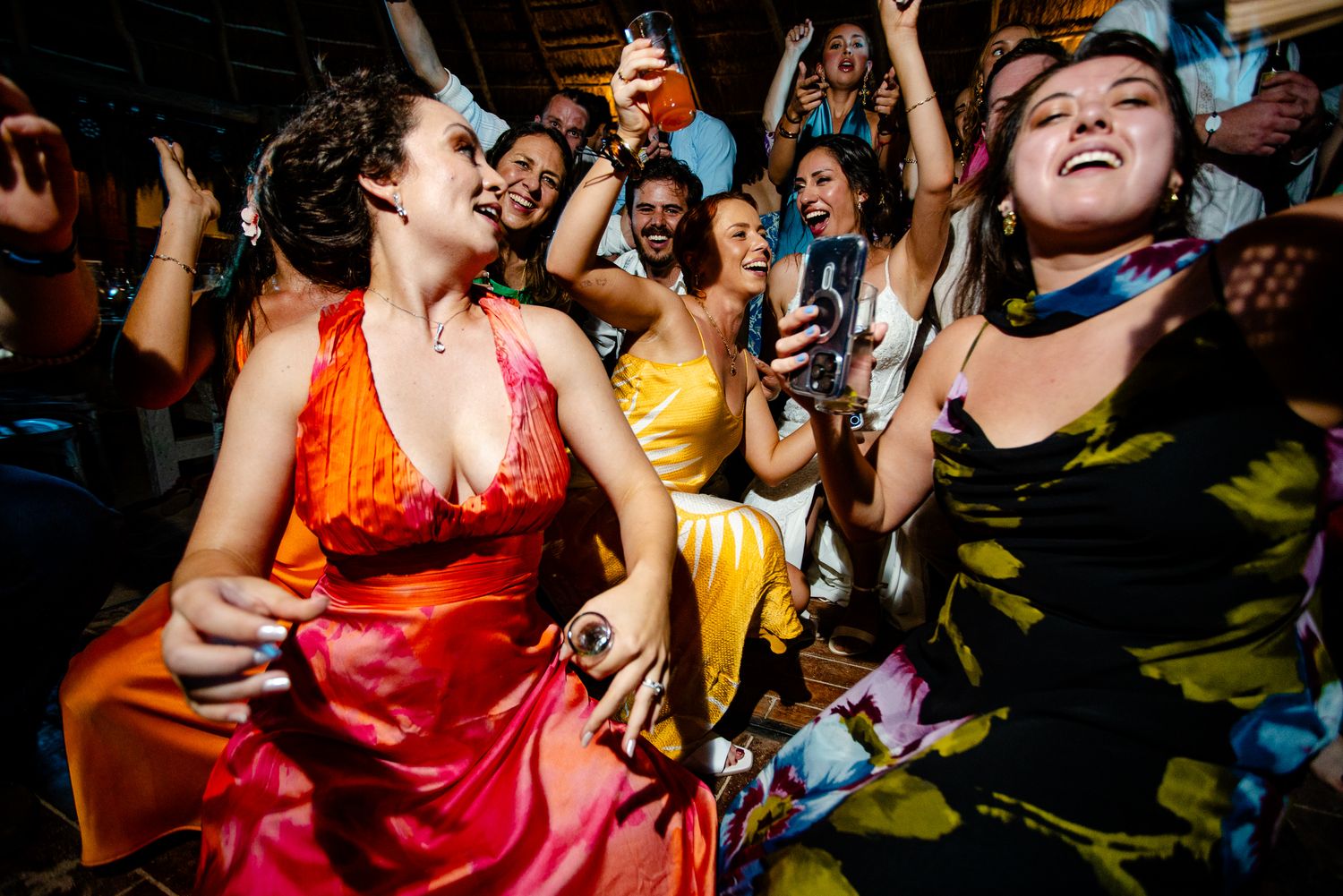 Joyful women in colorful dresses dancing and celebrating at a lively wedding reception party.