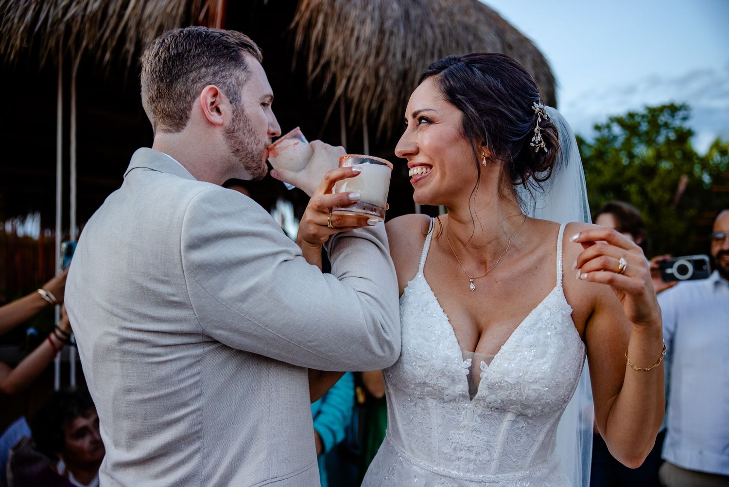 Bride and groom share a romantic drink together during outdoor beach wedding reception at dusk.