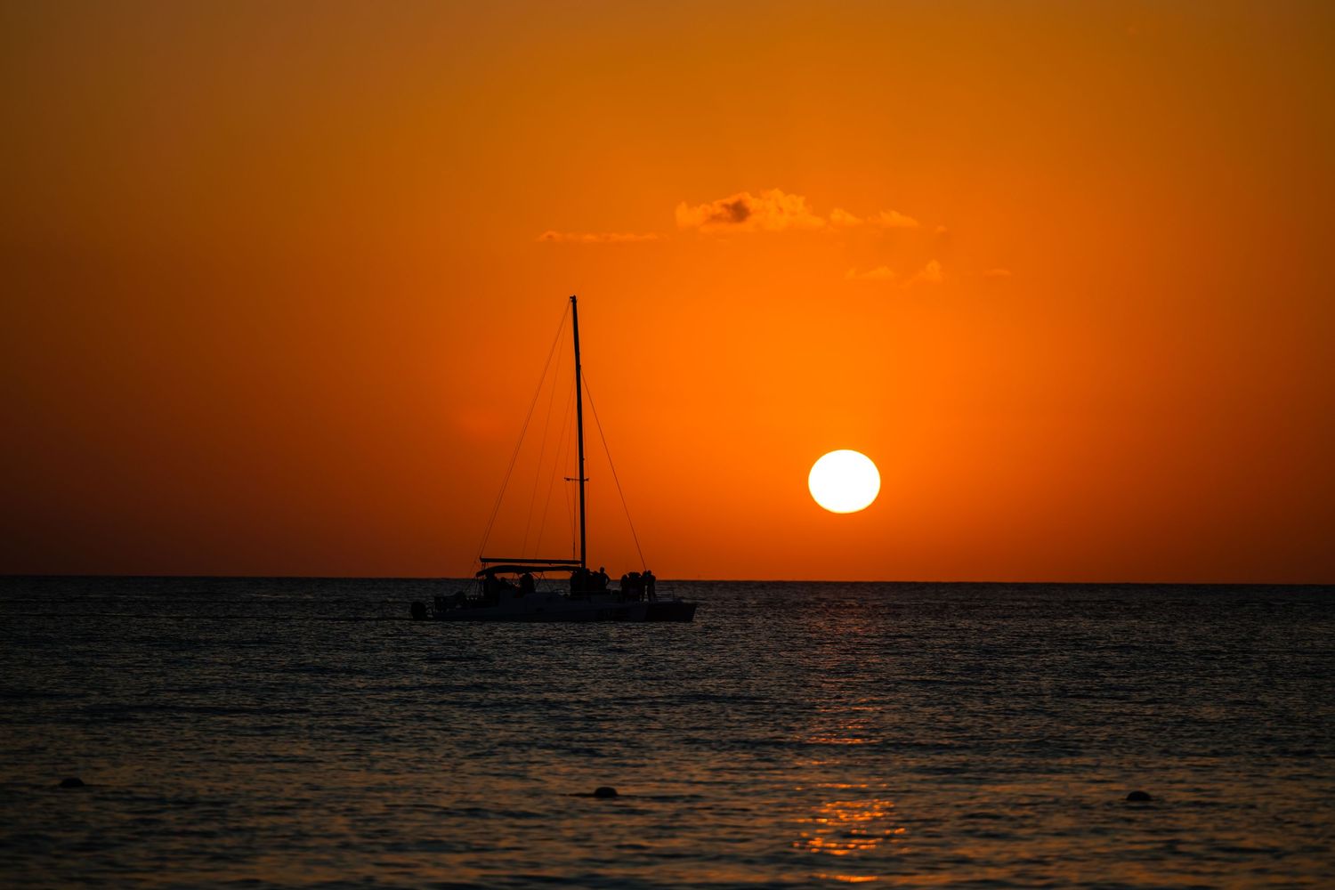 A dramatic orange sunset over calm ocean waters with a silhouetted pole visible on the horizon.