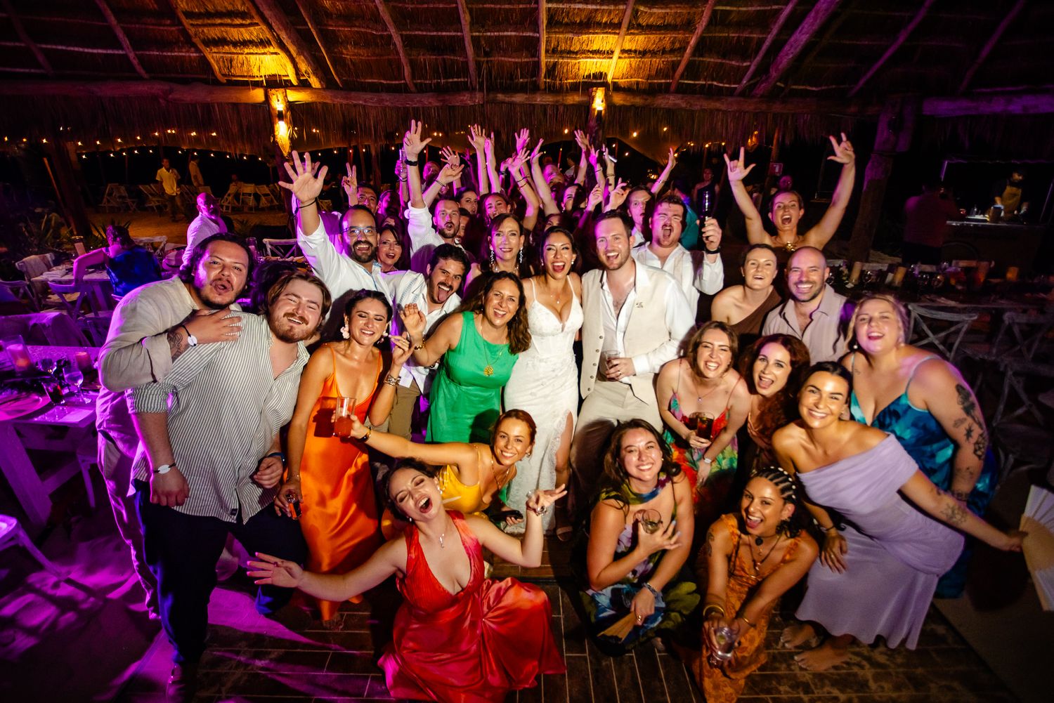 Large wedding party group photo with guests celebrating on a colorful dance floor at a tropical venue.