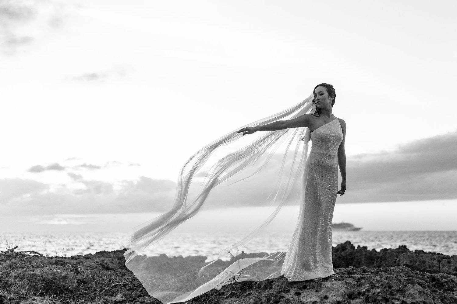 A flowing white wedding dress billows in the wind against a dramatic mountain landscape at sunset.