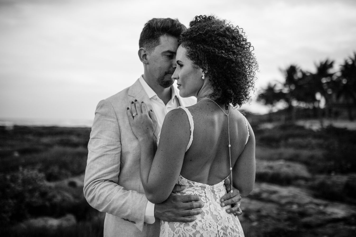 Black and white photo of a couple in wedding attire sharing an intimate moment outdoors near the ocean.