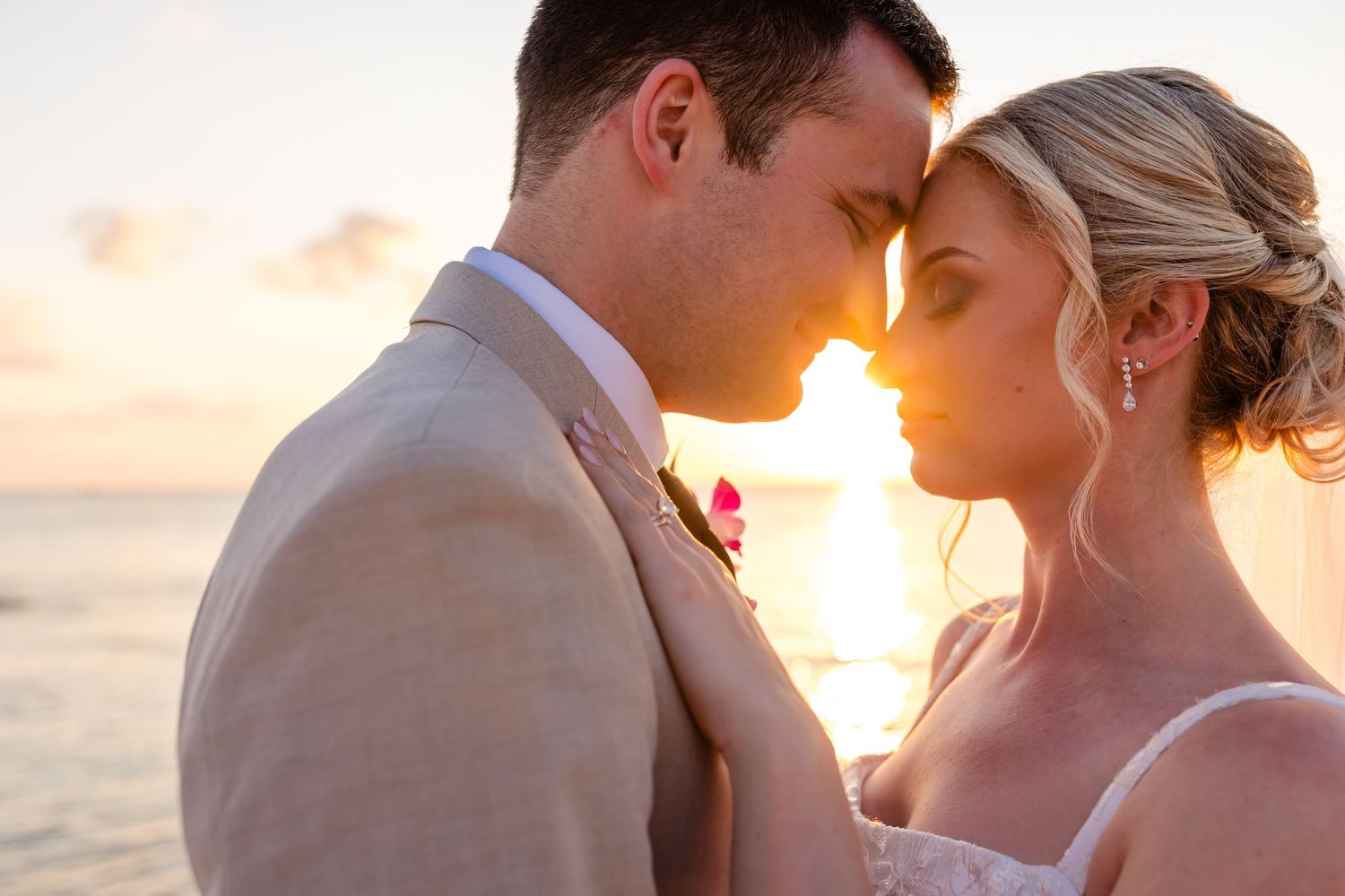 A couple shares a romantic kiss on the beach at sunset with the golden sun glowing behind them.