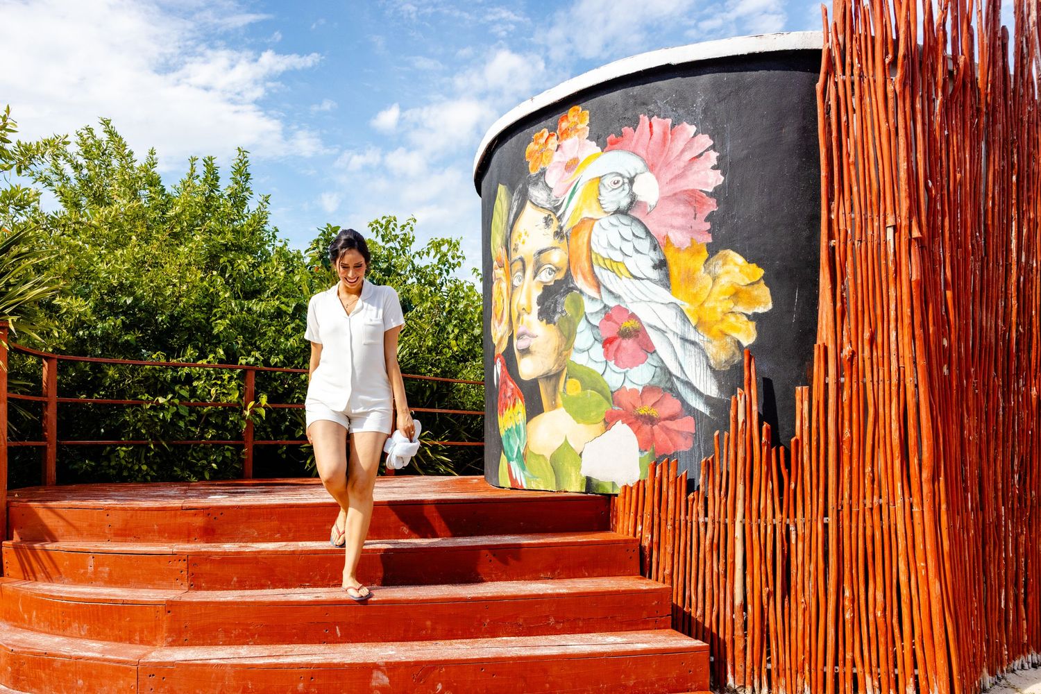 Woman walking down colorful red steps beside a vibrant floral mural on a curved wall outdoors.