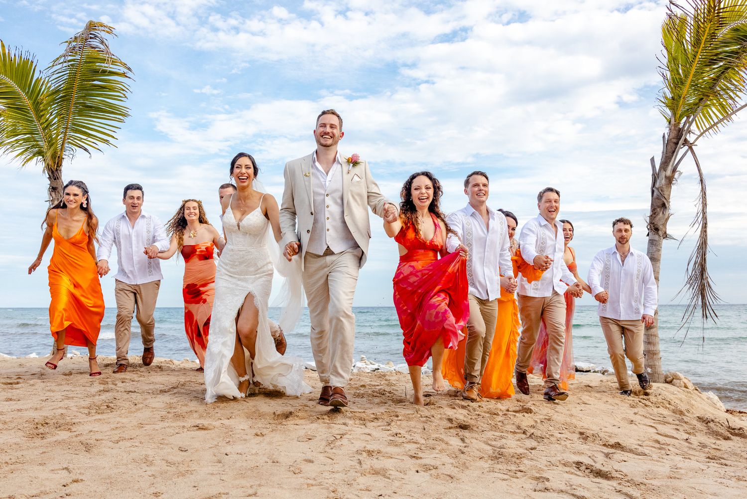 Wedding party celebrates on a tropical beach, bride and groom lead colorful bridesmaids and groomsmen under palm trees.