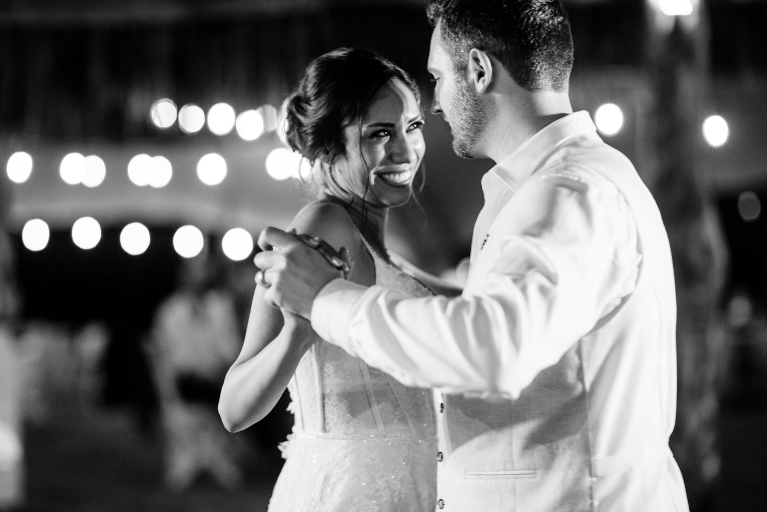 Bride and groom share first dance at wedding reception with bokeh lights.