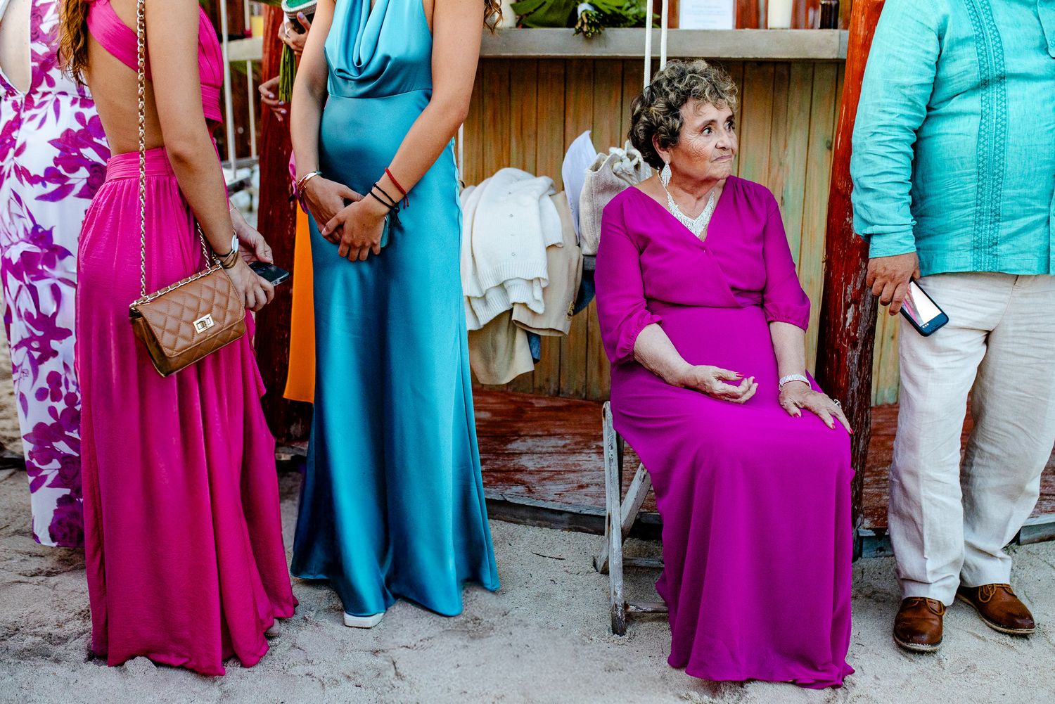Elegant wedding guests in colorful fuchsia and blue gowns at a beachside outdoor celebration.