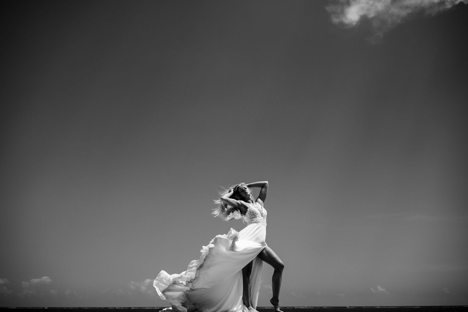 Black and white photo of a couple dancing outdoors under a dramatic sky, bride's dress flowing in the wind.
