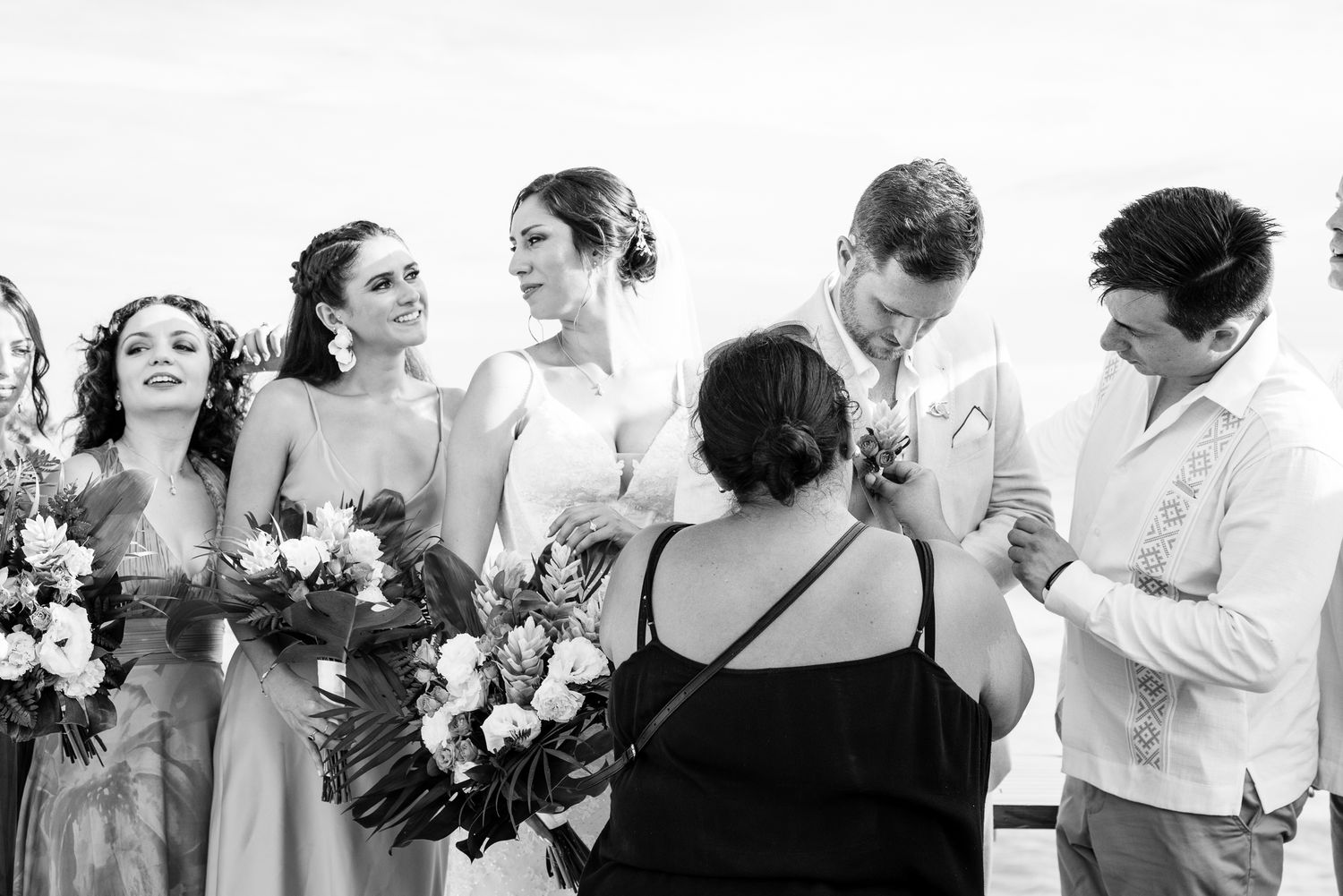 Black and white photo of a wedding party with bridesmaids holding bouquets as the couple shares a tender moment.
