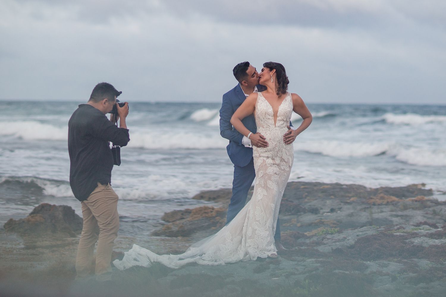 Photographer capturing couple's beach wedding portraits among ocean waves.
