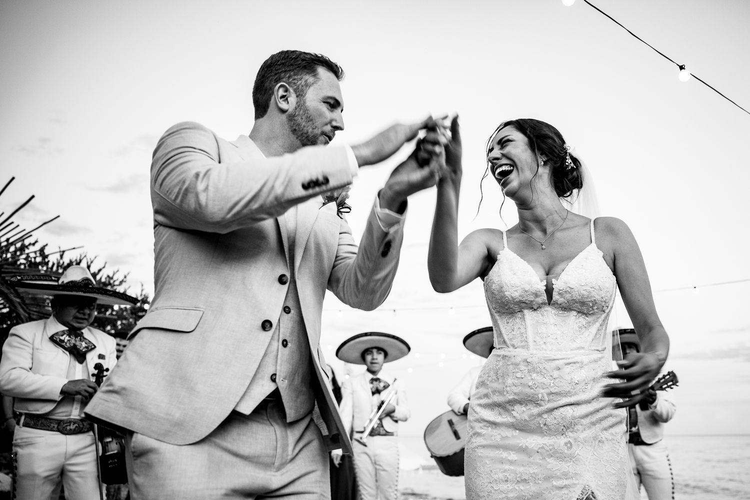 Black and white photo of laughing bride and groom celebrating with drinks at beach wedding.