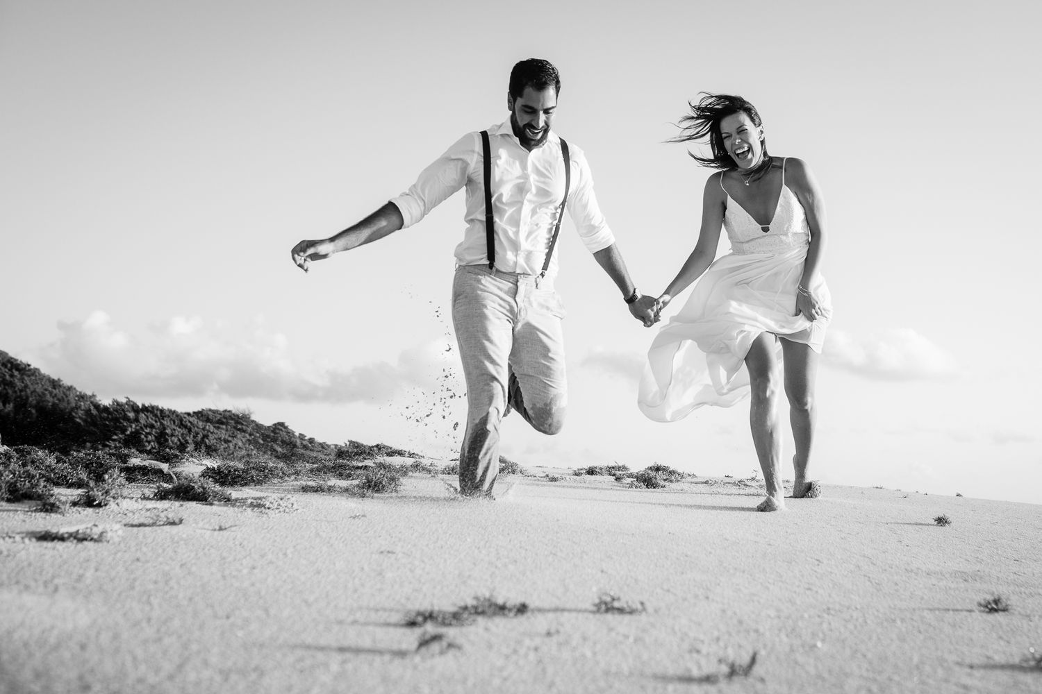 Joyful couple running and jumping on a sandy beach in black and white.