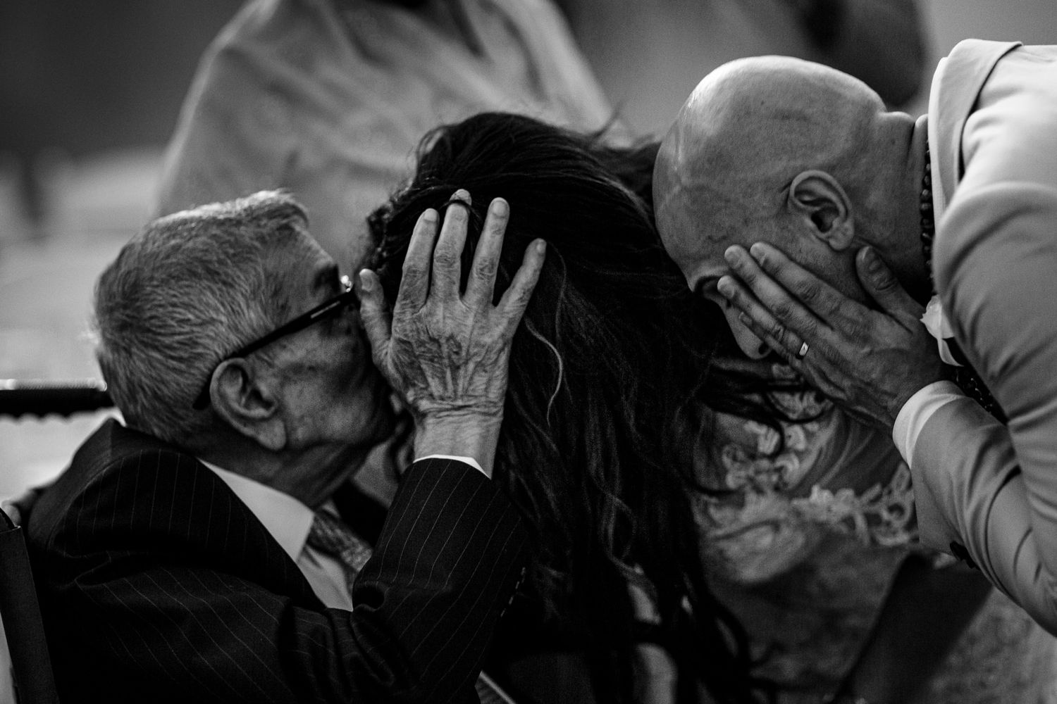 Black and white photo of elderly man kissing woman's cheek while another person covers their face with hands.