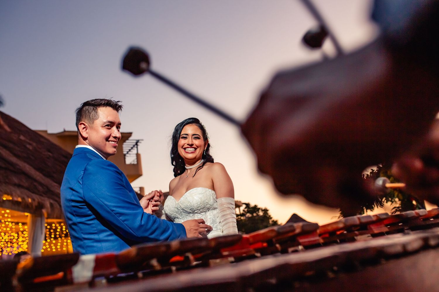 A couple sits together at a DJ booth during their wedding reception with soft lighting and equipment in the foreground.