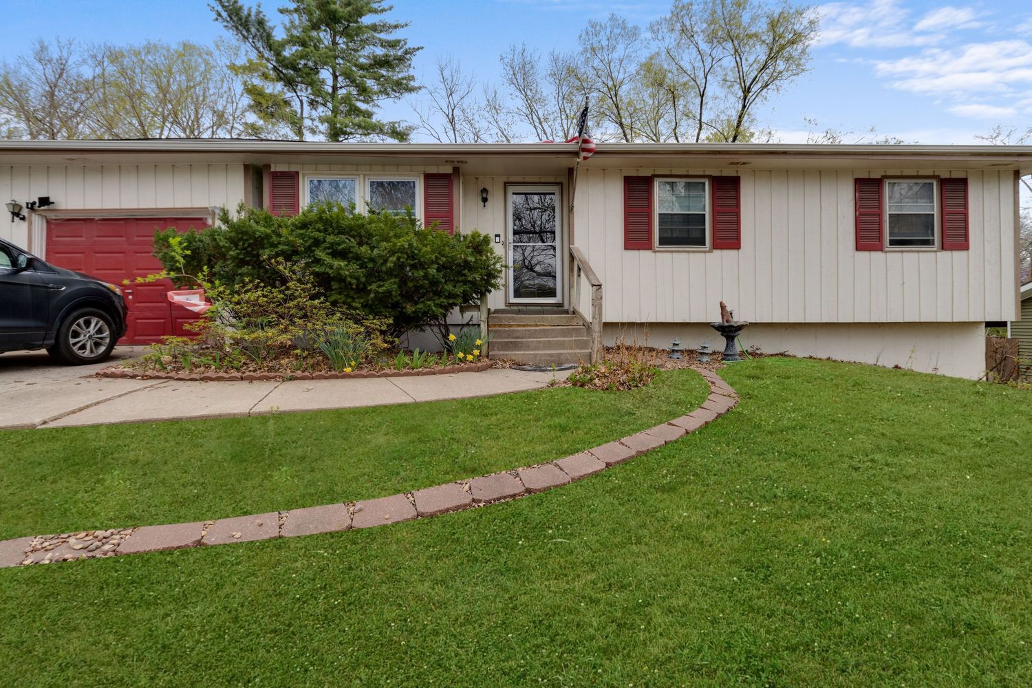 Ranch style house with white siding, red accent trim and curved landscaping border on green lawn.