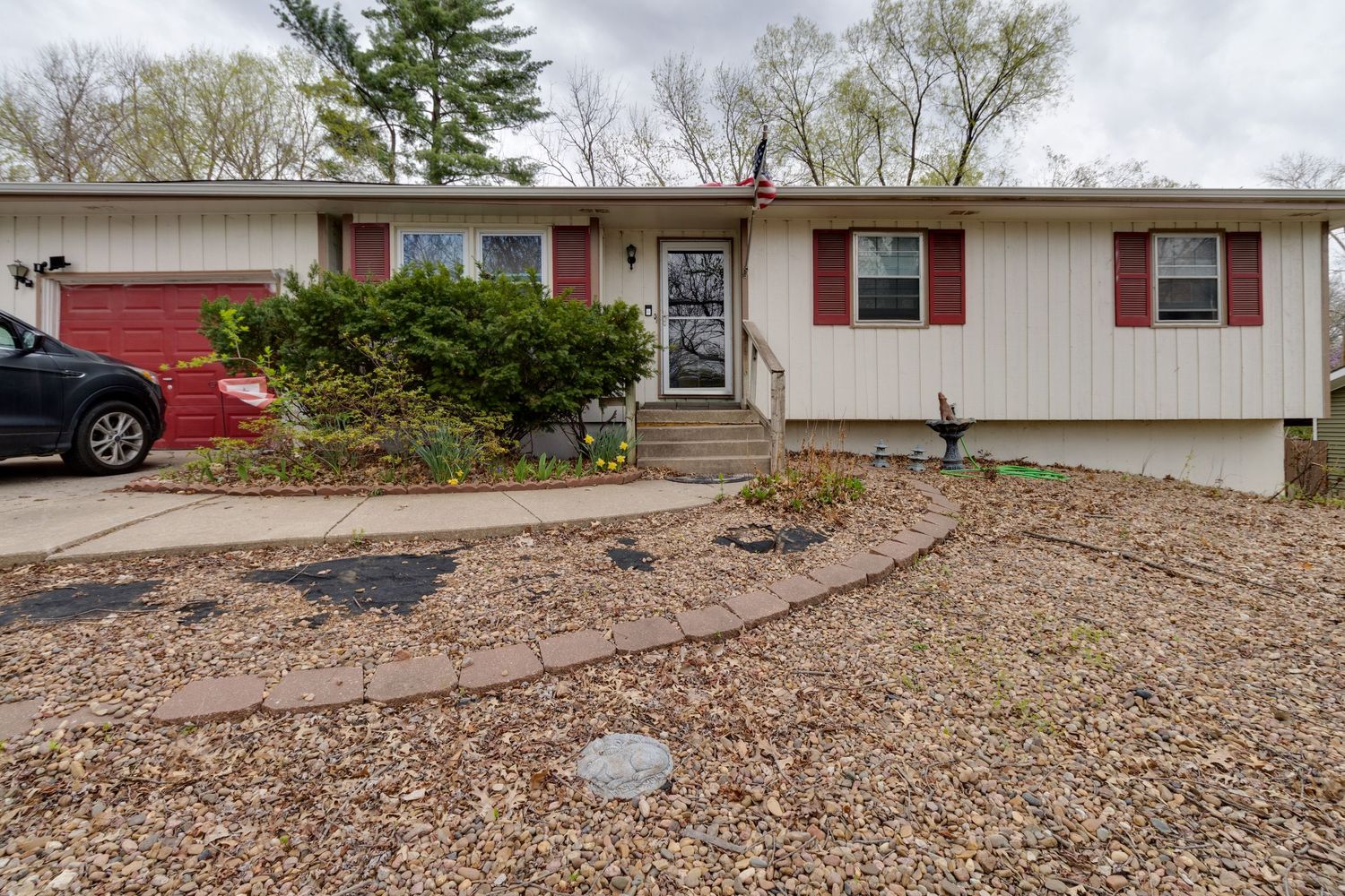 White ranch home with red trim and black shutters featuring curved landscaping path.