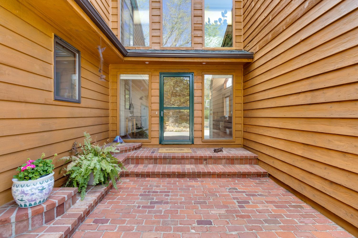 Modern courtyard entrance with brick pavers and cedar siding featuring glass door and planters.