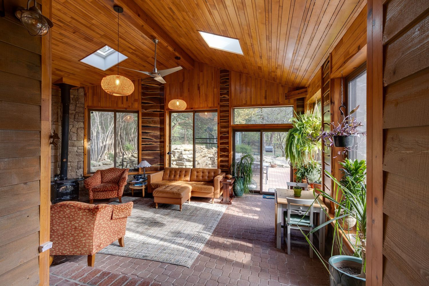 Sunlit wooden sunroom with skylights, comfortable seating, and abundant indoor plants.