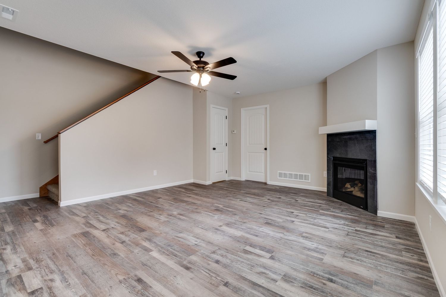 Empty living room with gray wood flooring, sloped ceiling, and built-in fireplace.