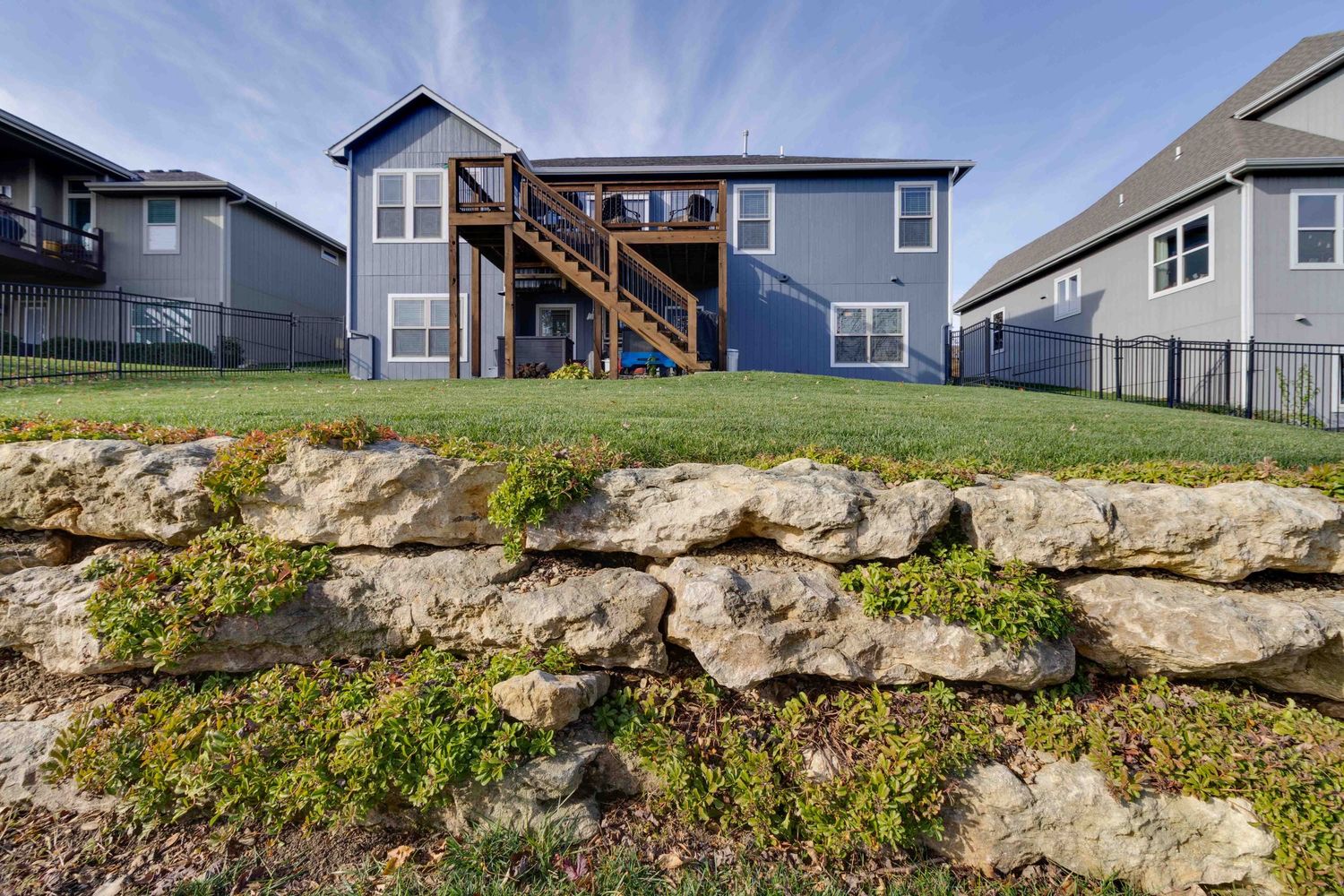 Modern blue two-story house with wooden staircase and natural stone retaining wall in the landscaping.