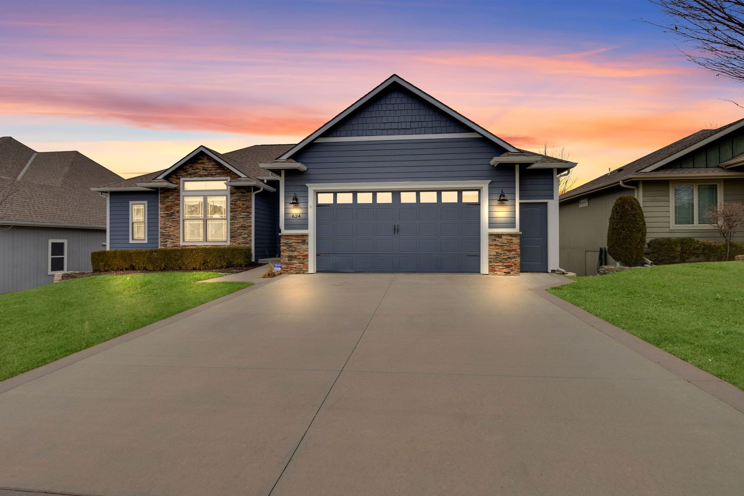 Blue house with stone accents and two-car garage at sunset with dramatic orange sky.