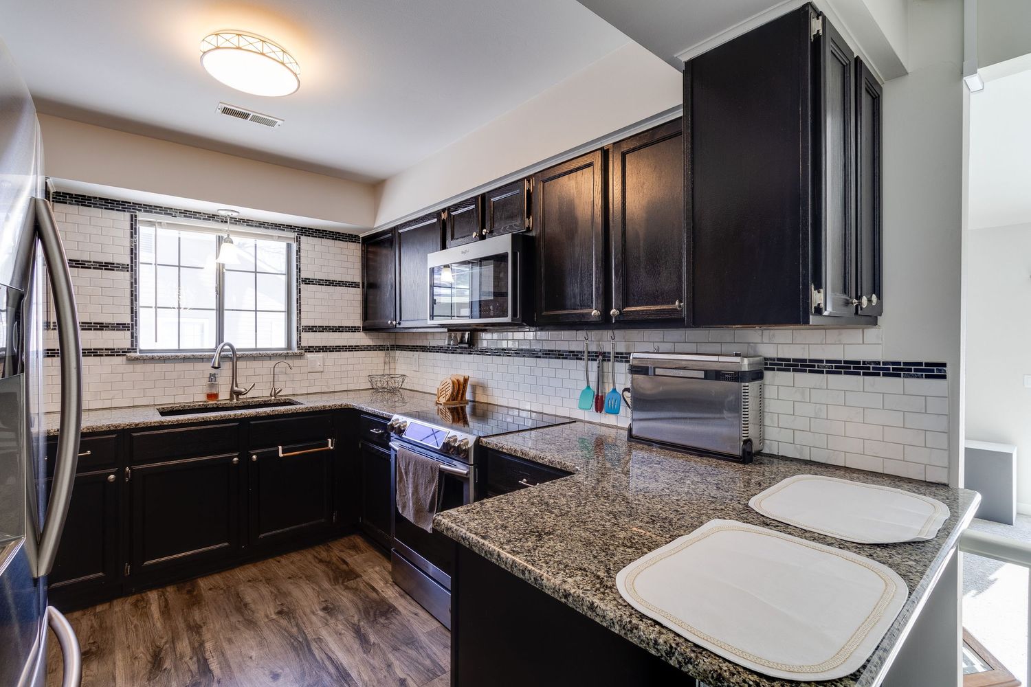 Contemporary kitchen featuring dark cabinets, granite countertops, and stainless steel appliances.