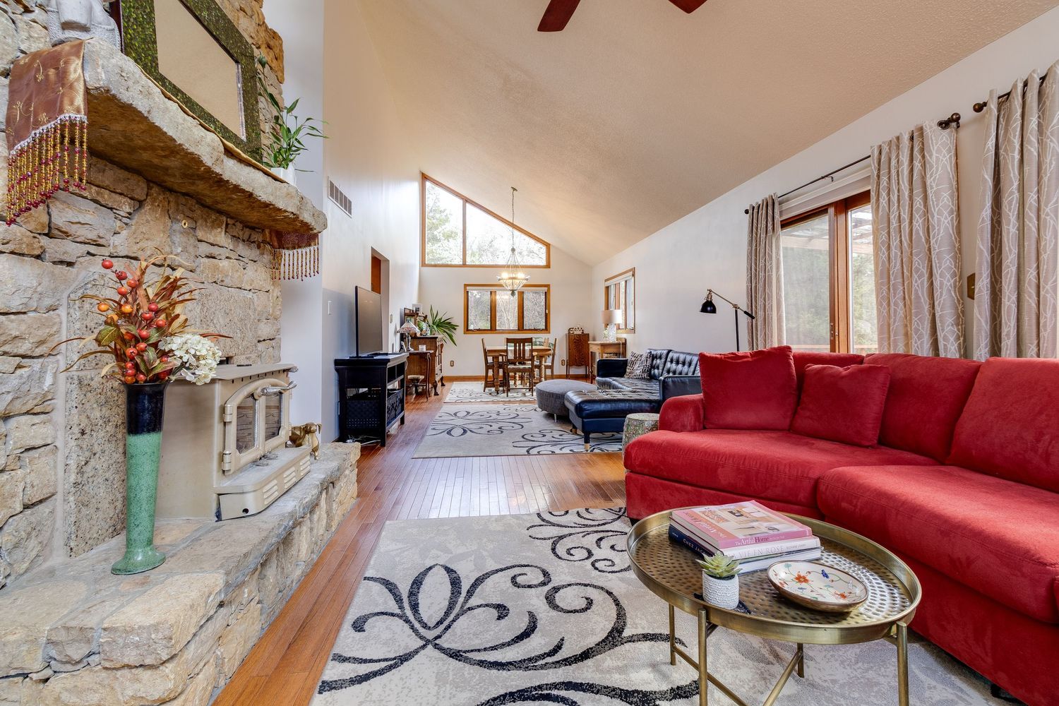 Living room with stone fireplace, vaulted ceiling, and curved red sectional sofa on patterned rug.