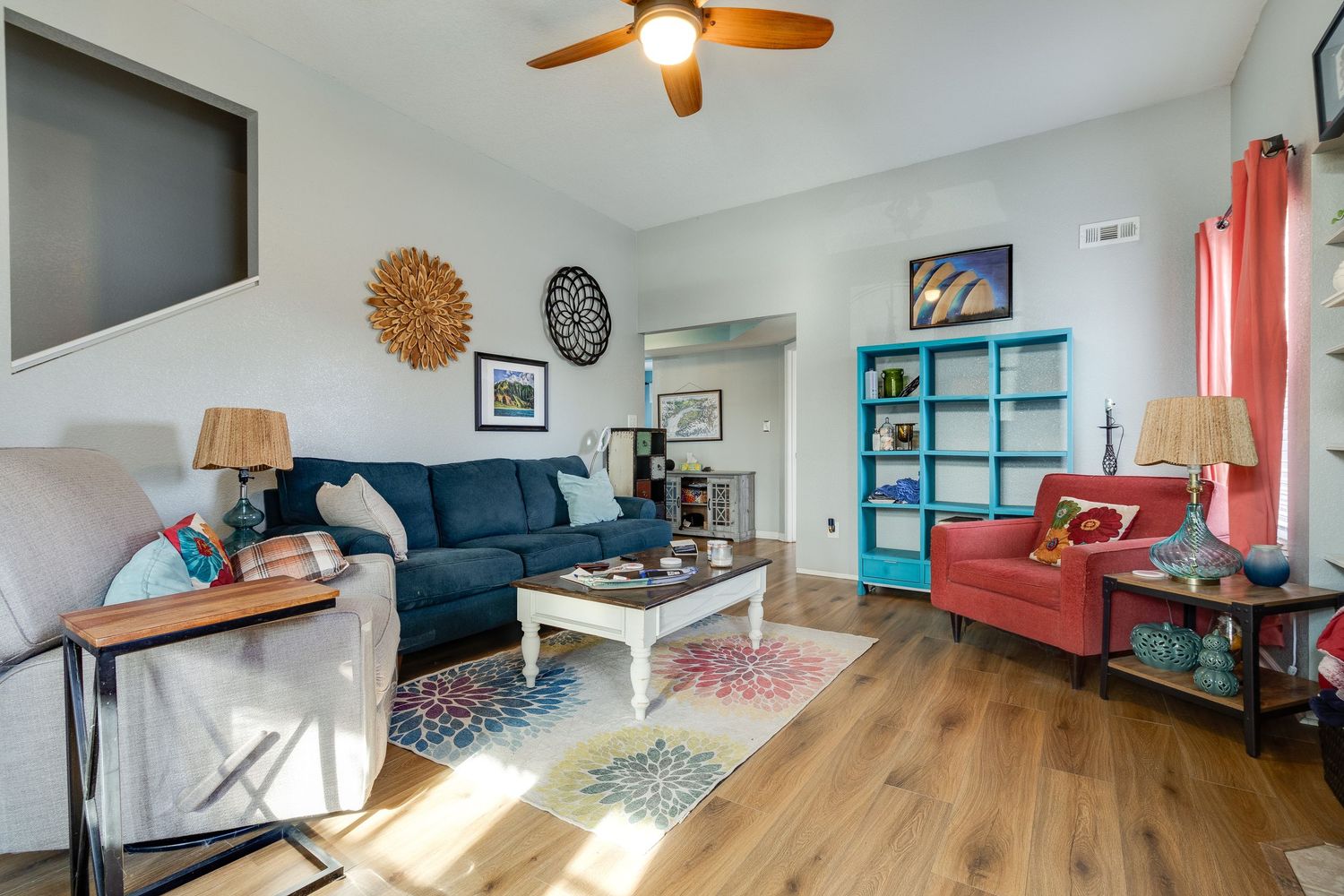 Modern living room with blue sofa, turquoise bookshelf, and hardwood floors.