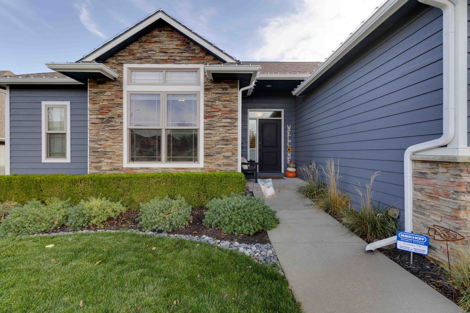Modern craftsman home with stone accents, blue siding, and landscaped front yard.
