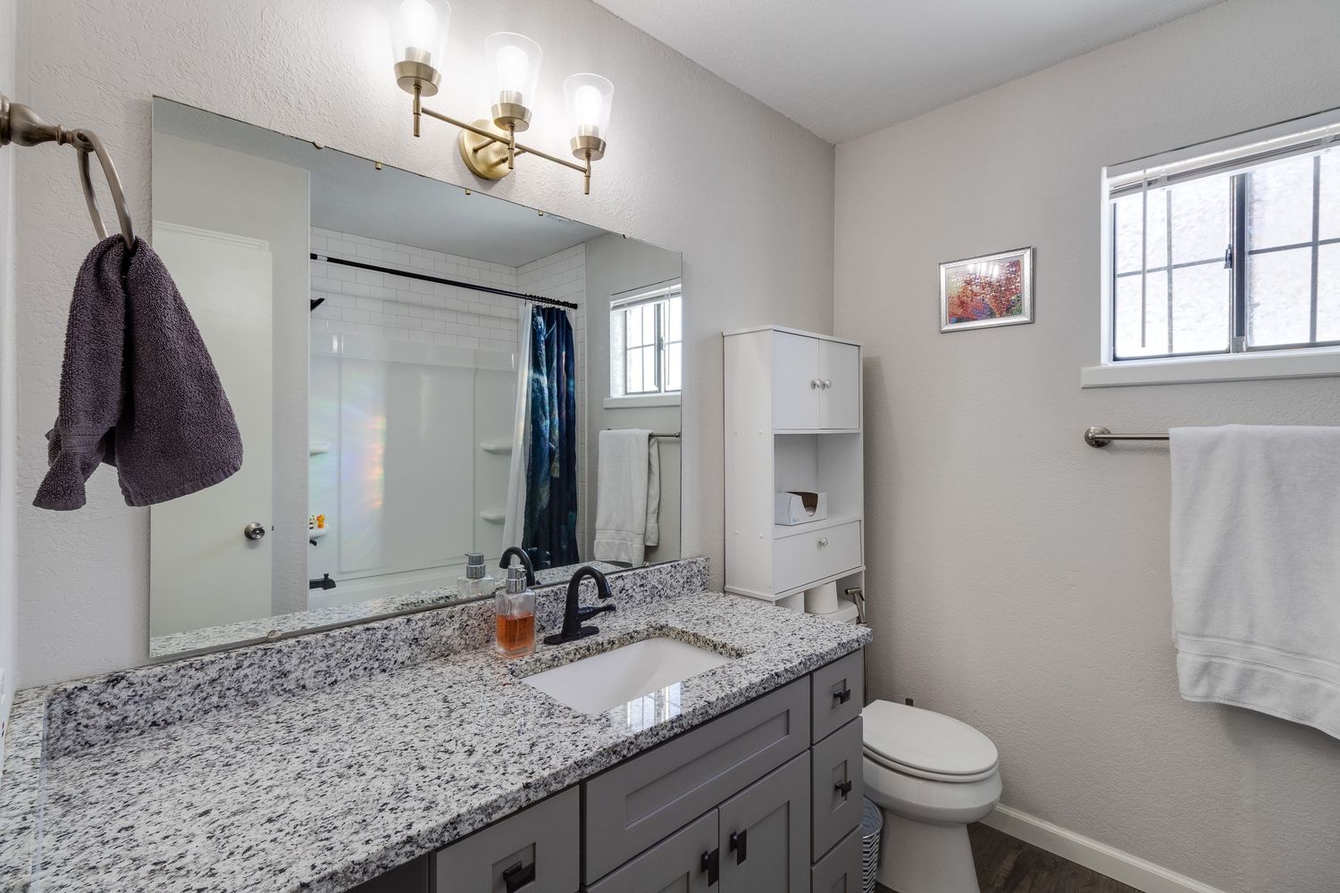 Updated bathroom featuring granite countertop vanity, large mirror, and modern light fixtures.