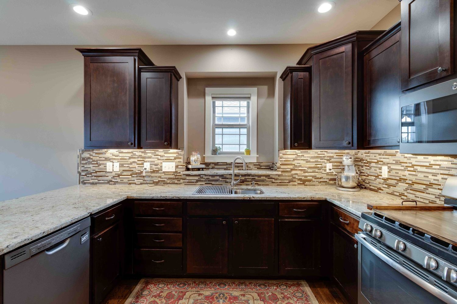 U-shaped kitchen with rich brown cabinetry, stone backsplash, and granite countertops showcasing contemporary design.