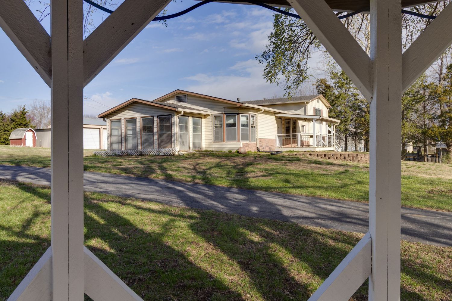 Ranch-style house viewed through white pergola posts with manicured lawn.