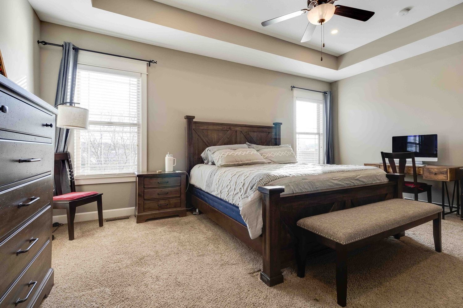 Master bedroom with tray ceiling, dark wood furniture, and bench at foot of bed.