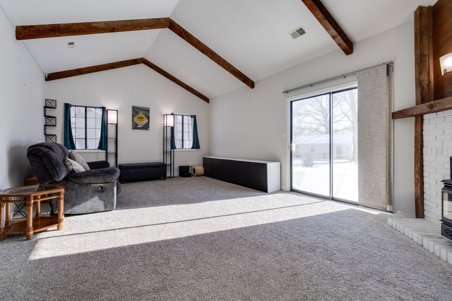 Spacious living room with vaulted ceiling, exposed beams, and sliding glass doors leading outside.
