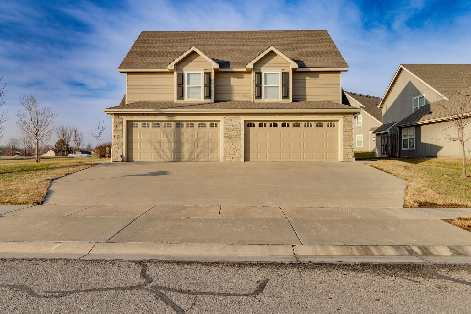 Large suburban house with tan siding and triple dormer windows above three-car garage.